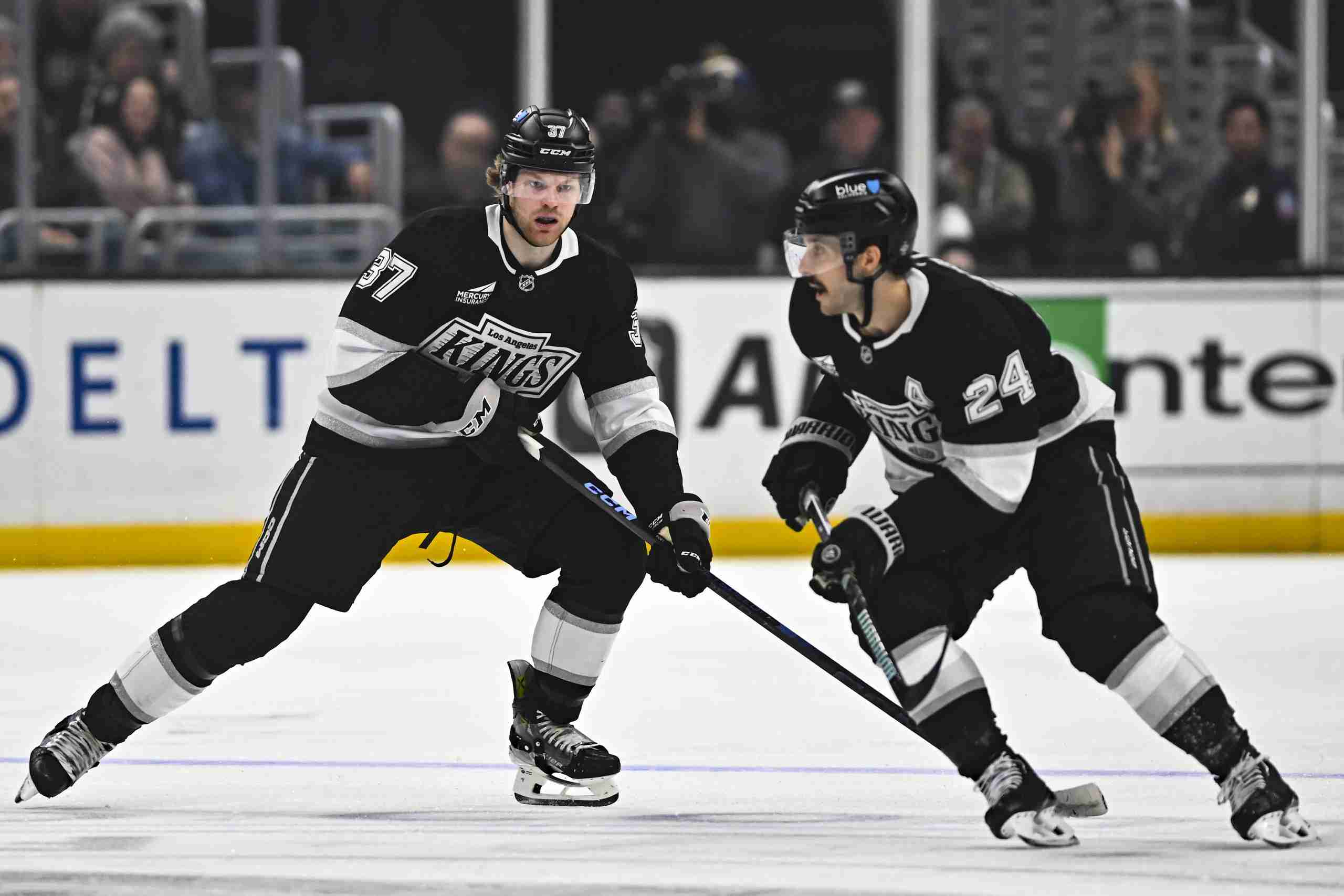 Mar 22, 2025; Los Angeles, California, USA; Los Angeles Kings left wing Warren Foegele (37) moves the puck with center Phillip Danault (24) against the Carolina Hurricanes during the second period at Crypto.com Arena. Mandatory Credit: Jonathan Hui-Imagn Images
